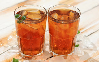 Glass of iced herbal tea with lemon and herbs on a summer table, sunlight in the background.