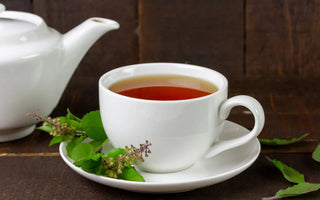 A cup of herbal tea with steam rising, surrounded by passionflower, tulsi leaves, and lemongrass on a wooden tray